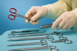 Close-up of a surgeon’s gloved hands selecting red-handled forceps from a sterile table of surgical instruments in a clinical setting